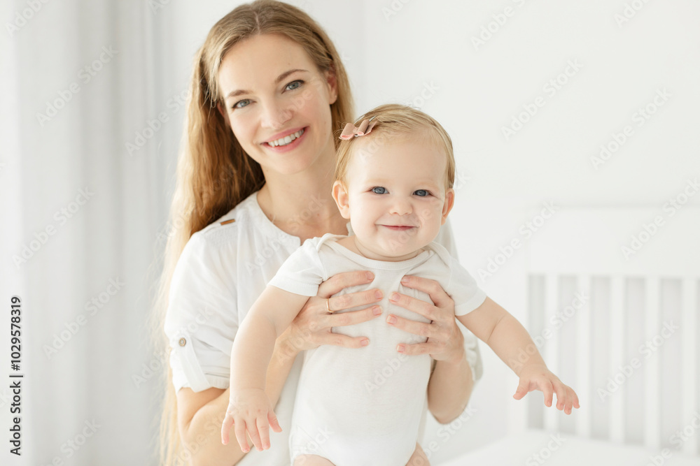 Maternal love and care concept. Beautiful European mother with baby girl having fun on the bed in bright bedroom, happy motherhood with maternity leave Maternal love and care concept. Beautiful European mother with baby girl having fun on the bed in bright bedroom, happy motherhood with maternity leave