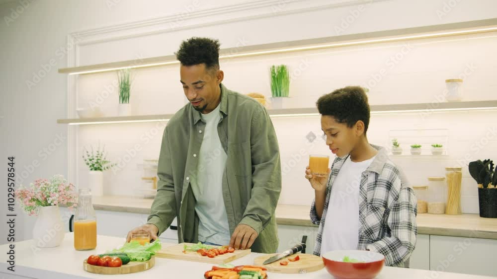 The happy African American father and son drink orange juice in the kitchen after preparing dinner The happy African American father and son drink orange juice in the kitchen after preparing dinner