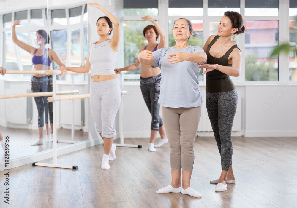 Obraz premium Adult female trainer helps beginner women perform ballet movements correctly