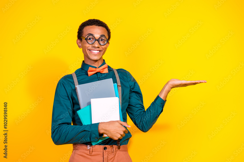 Photo portrait of handsome young guy copybooks hold empty space dressed stylish suit garment isolated on yellow color background Photo portrait of handsome young guy copybooks hold empty space dressed stylish suit garment isolated on yellow color background