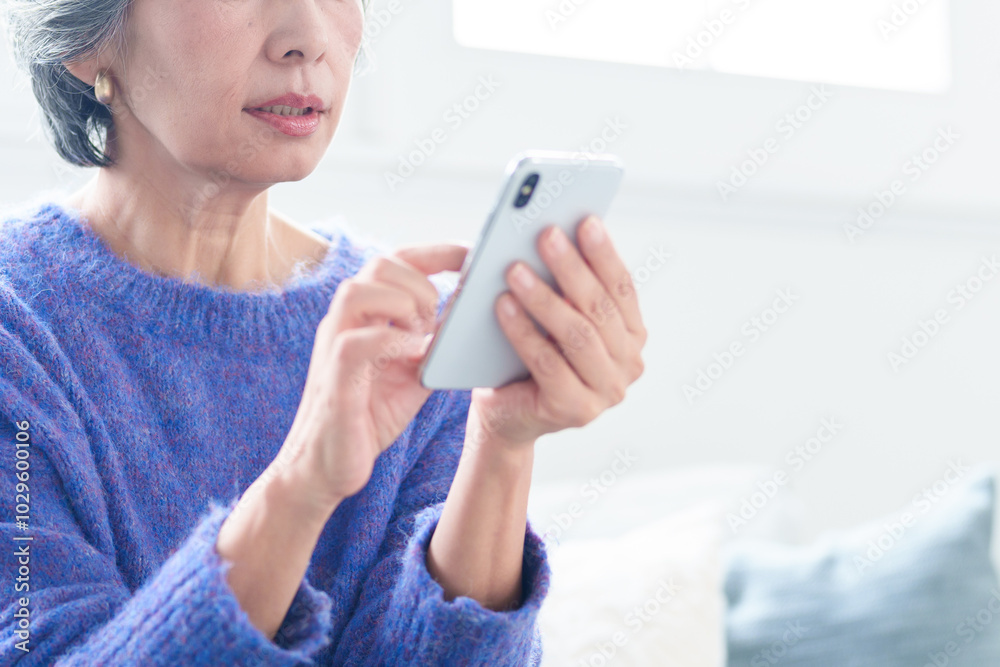 リビングでスマートフォンを使う中高年の女性 リビングでスマートフォンを使う中高年の女性