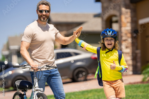 Happy Fathers day. Father and son in bike helmet for learning to ride bicycle at park. Father helping son cycling. Father and son on the bicycle on summer day. Kid son trying to ride bike with father. photo