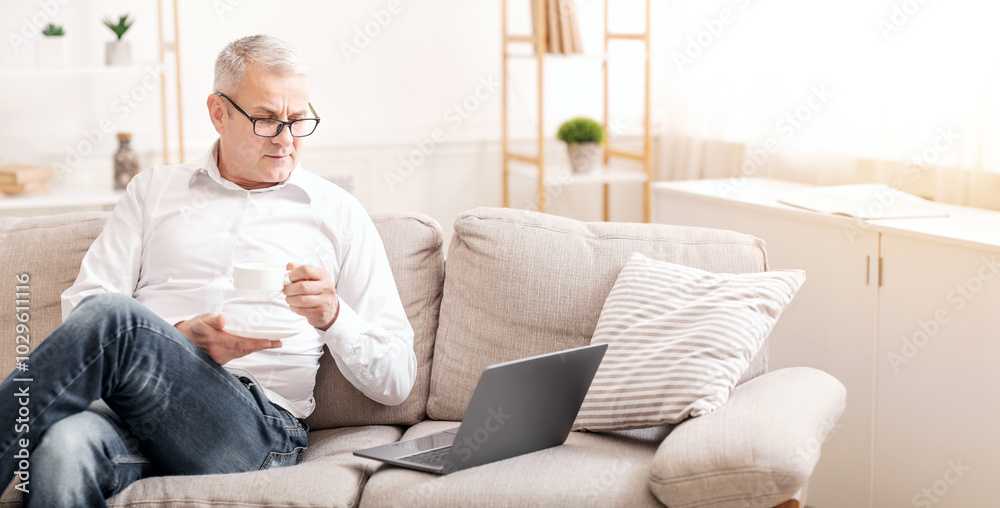 In The Morning. Senior Man Using Laptop Computer Having Coffee Sitting On The Couch At Home, Copyspace In The Morning. Senior Man Using Laptop Computer Having Coffee Sitting On The Couch At Home, Copyspace