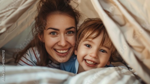 Cheerful family enjoying time together, with a mother and young son playing and smiling inside a blanket fort during the evening