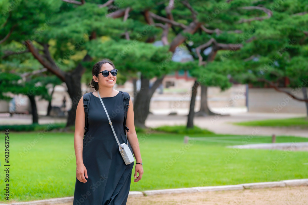 Young happy Latina woman in a black dress and backpack smiling in in Deoksugung Palace garden, Seoul, South Korea. Young happy Latina woman in a black dress and backpack smiling in in Deoksugung Palace garden, Seoul, South Korea.