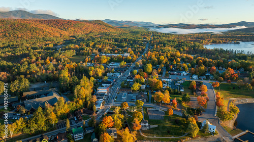 Aerial view of Schroon Lake, NY, with vibrant autumn colors, tree-lined streets, and surrounding Adirondack Mountains, showcasing the small town's scenic charm and peaceful lakeside setting.