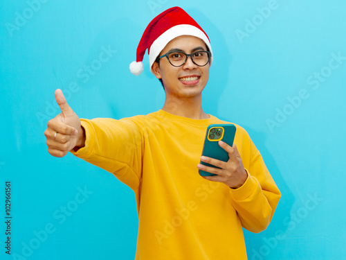 asian man wearing christmas hat posing by holding mobile phone. photo