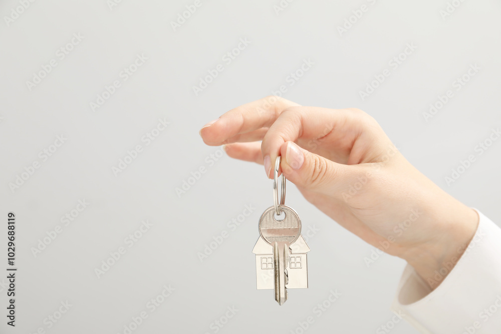 Woman holding key with keychain on light grey background, closeup. Space for text Woman holding key with keychain on light grey background, closeup. Space for text