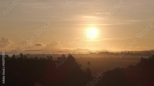 Aerial ascend above dawn breaking over tropical forests and misty fields, soft morning light fills the sky over the valley. Surigao City, Philippines. 