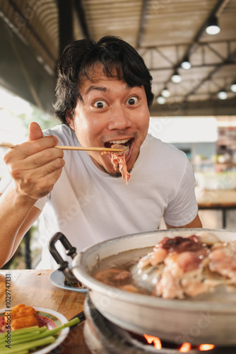 Happy and excited Asian face man eating Moo Kra Ta or Thai BBQ buffet. photo