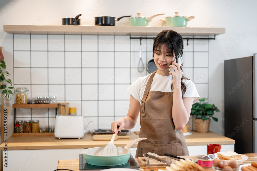 A charming Asian woman is talking on the phone while cooking in the kitchen. A charming Asian woman is talking on the phone while cooking in the kitchen.