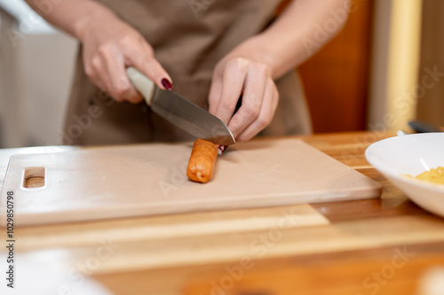 A close-up of a woman cutting a sausage on a cutting board at a kitchen island.