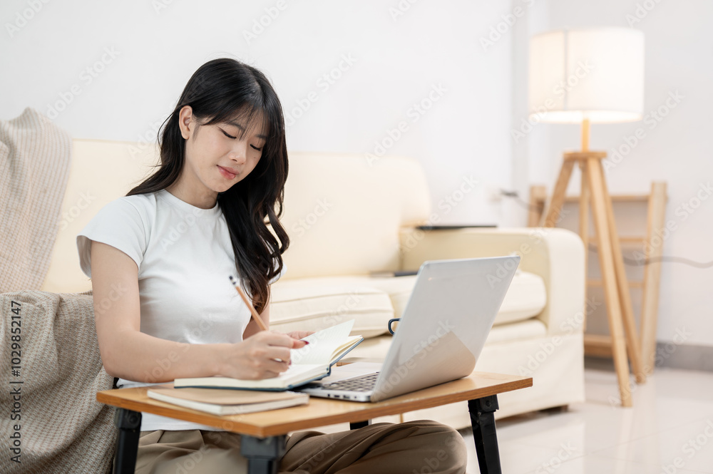 A pretty Asian female college student sitting on the living room floor and doing homework. A pretty Asian female college student sitting on the living room floor and doing homework.