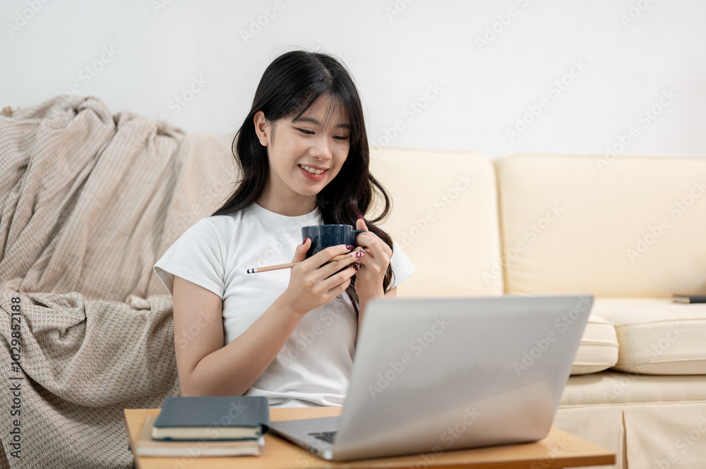 A pretty Asian female college student is studying online at home, watching a lesson on her laptop. A pretty Asian female college student is studying online at home, watching a lesson on her laptop.