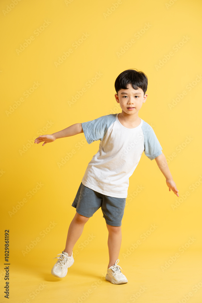 Full body image of asian kid boy wearing summer clothes posing on yellow background Full body image of asian kid boy wearing summer clothes posing on yellow background