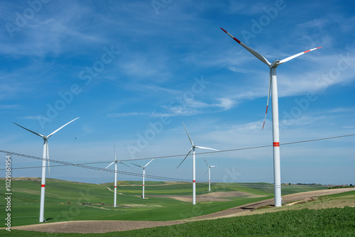 Wind turbines and power lines in a green agricultural landscape seen in Italy