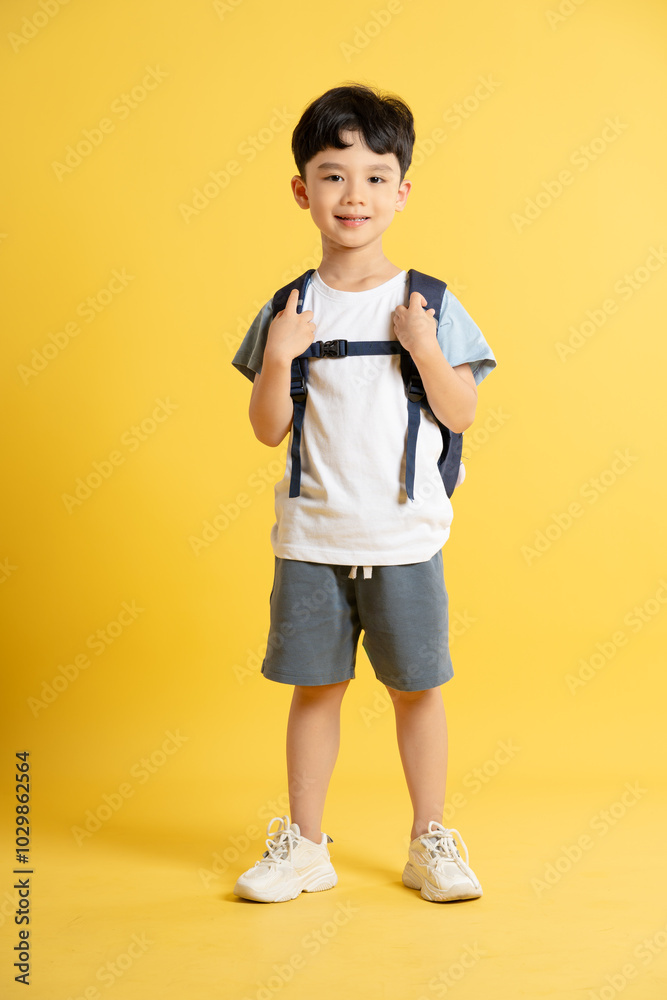 Full body image of an Asian boy wearing a school backpack and posing on a yellow background Full body image of an Asian boy wearing a school backpack and posing on a yellow background