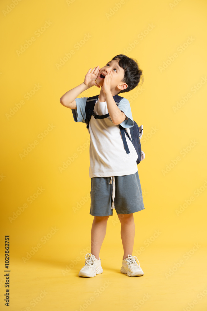Full body image of an Asian boy wearing a school backpack and posing on a yellow background Full body image of an Asian boy wearing a school backpack and posing on a yellow background