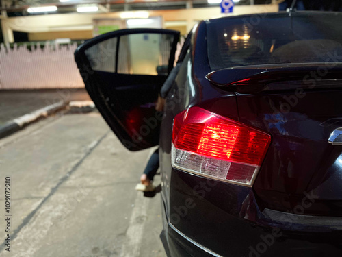 parked black car with its rear door open and red brake lights illuminated. The car is parked on a street at night, with some exterior lighting in the background, car on the road, car emergency