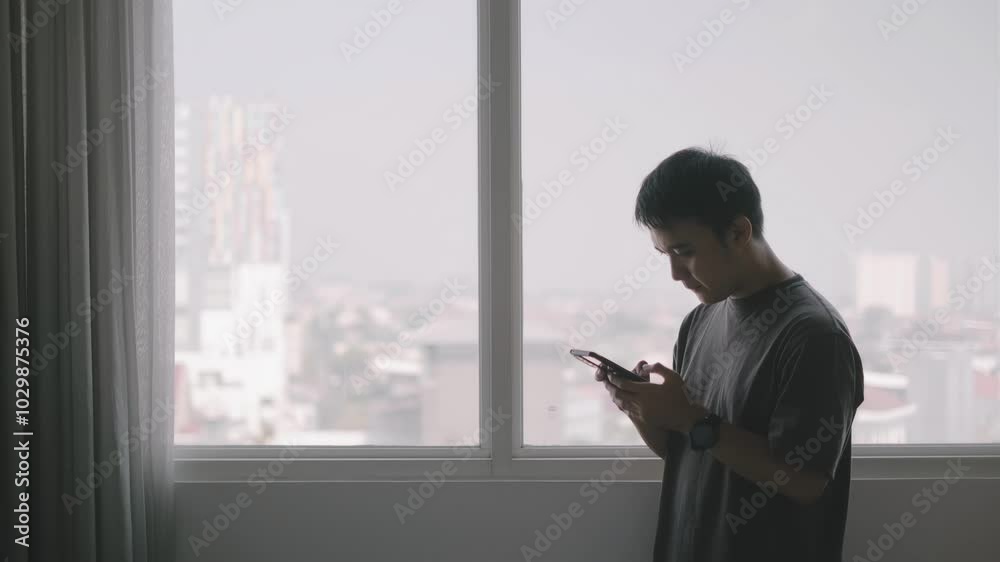 Young Asian man using a smartphone in the apartment with bokeh background