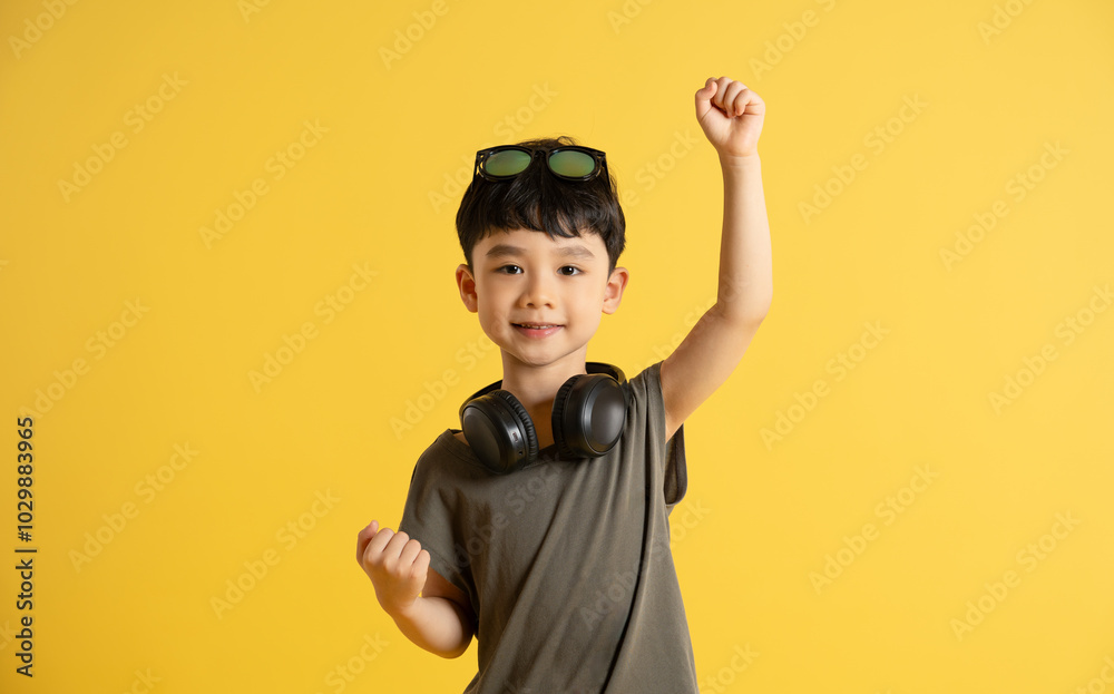 Portrait of an Asian boy wearing a tank top, headphones, and sunglasses posing on a yellow background Portrait of an Asian boy wearing a tank top, headphones, and sunglasses posing on a yellow background