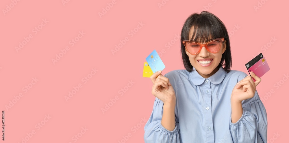 Beautiful happy young woman holding credit cards on pink background with space for text Beautiful happy young woman holding credit cards on pink background with space for text