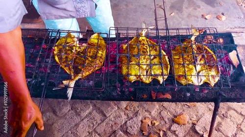 Grilling fish over coconut shell coals, smoke billowing from the small fire photo