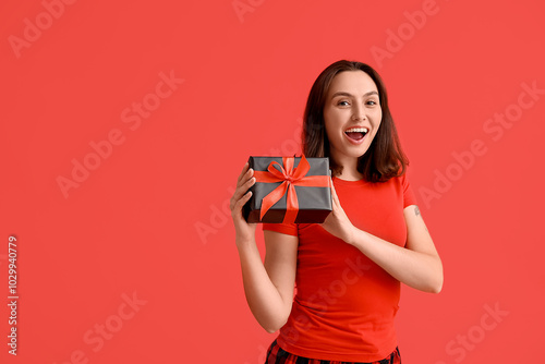 Beautiful young woman in pajamas with gift box on red background