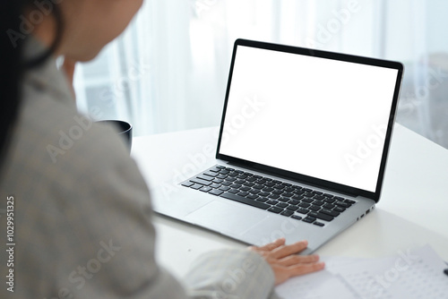 A woman is sitting at a desk with a laptop open in front of her. The laptop screen is blank.