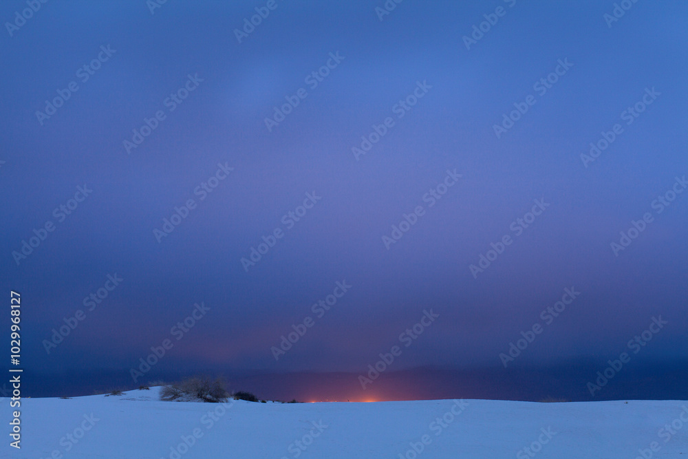 Naklejka premium Distant orange lights against deep blue evening sky
