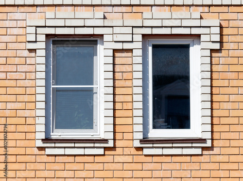 Two windows with white frames sit on a brick wall