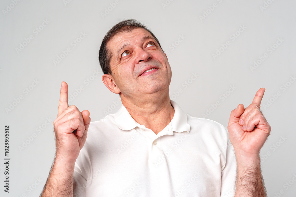Man in a white shirt pointing upwards with a thoughtful expression in a neutral setting Man in a white shirt pointing upwards with a thoughtful expression in a neutral setting