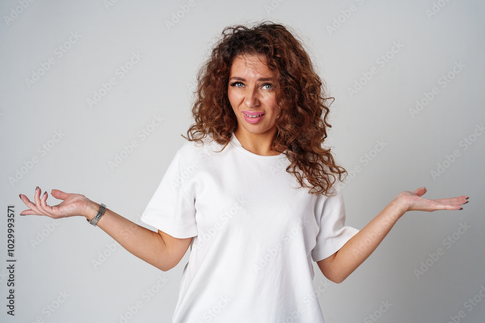 Cheerful woman with curly hair poses with open arms in a white shirt against a plain background Cheerful woman with curly hair poses with open arms in a white shirt against a plain background