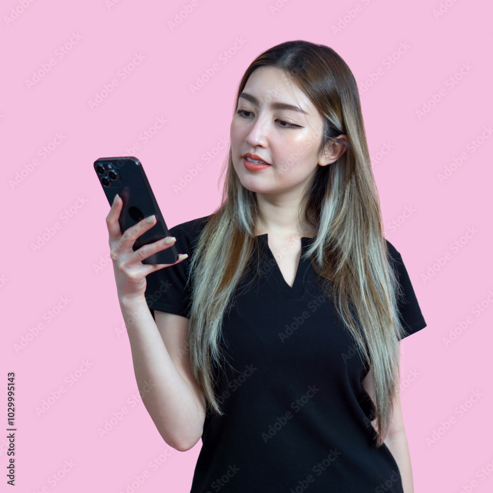 Young asian woman in casual clothing, holding and looking at a smartphone. Portrait on a simple pink background with studio light. Isolated