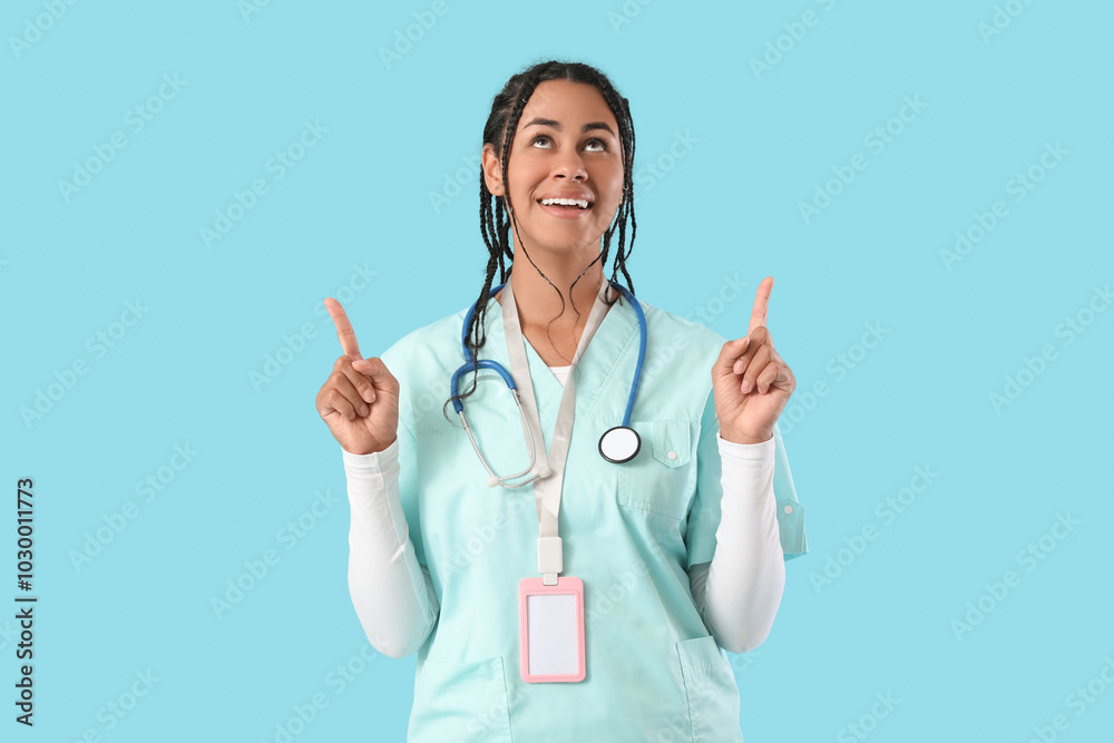 Young African-American female doctor with stethoscope pointing at something on blue background Young African-American female doctor with stethoscope pointing at something on blue background