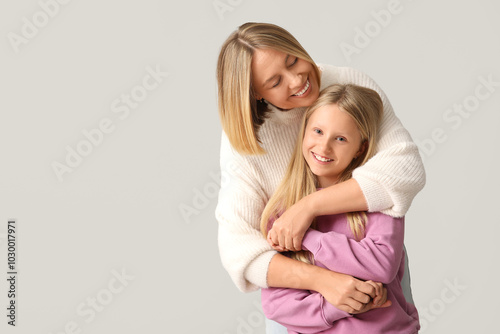 Beautiful woman hugging her cute daughter in stylish sweaters on grey background