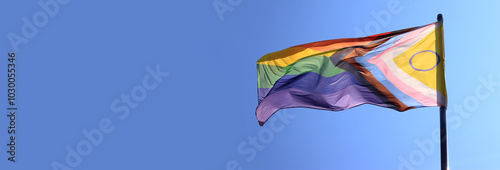 Intersex-inclusive redesign of the Progress Pride Flag. Rainbow LGBT flag against a blue sky. Flag fluttering in the wind. An abbreviation that stands for lesbian, gay, bisexual, transgender