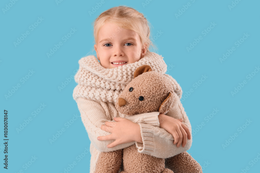 Cute little girl in winter clothes with toy bear on blue background Cute little girl in winter clothes with toy bear on blue background