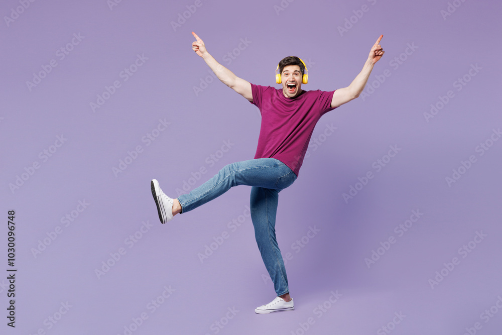Obraz premium Full body young happy man he wear violet t-shirt casual clothes listen to music in headphones raise up hands dance isolated on plain pastel light purple background studio portrait. Lifestyle concept.