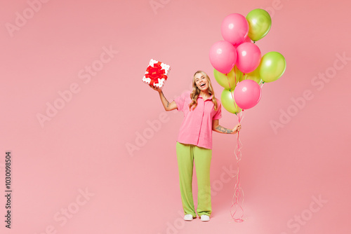 Full body young woman wears shirt celebrating birthday holiday and hold bunch of colorful air balloons hold present box with gift ribbon bow isolated on plain light pink background. Lifestyle concept.