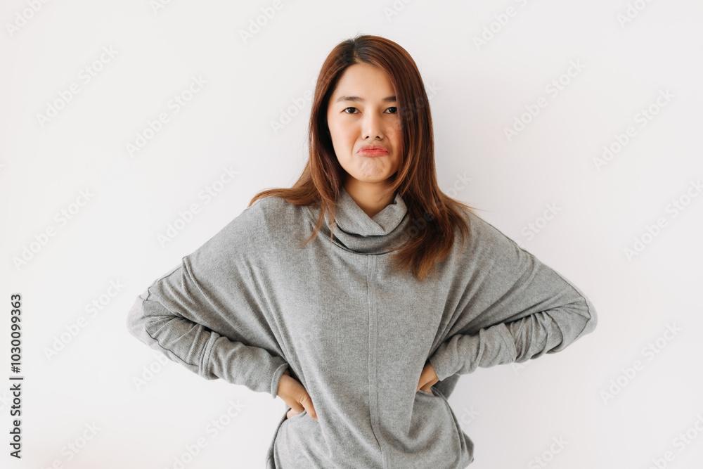 Bored face of asian Thai woman wear grey sweater, pursing mouth and thumbs down, giving bad negative, boring, dislike isolated over white wall.