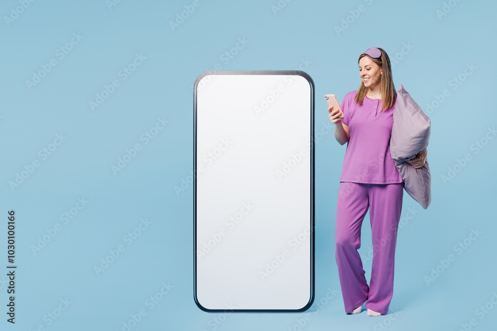 Full body calm young woman wears purple pyjamas jam sleep eye mask rest relax at home big huge blank screen area use mobile cell phone isolated on plain blue background. Good mood night nap concept. Full body calm young woman wears purple pyjamas jam sleep eye mask rest relax at home big huge blank screen area use mobile cell phone isolated on plain blue background. Good mood night nap concept.