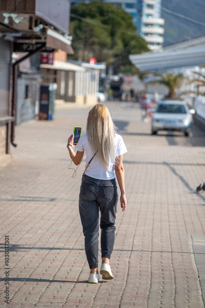 A woman is walking down a sidewalk while holding a cell phone A woman is walking down a sidewalk while holding a cell phone