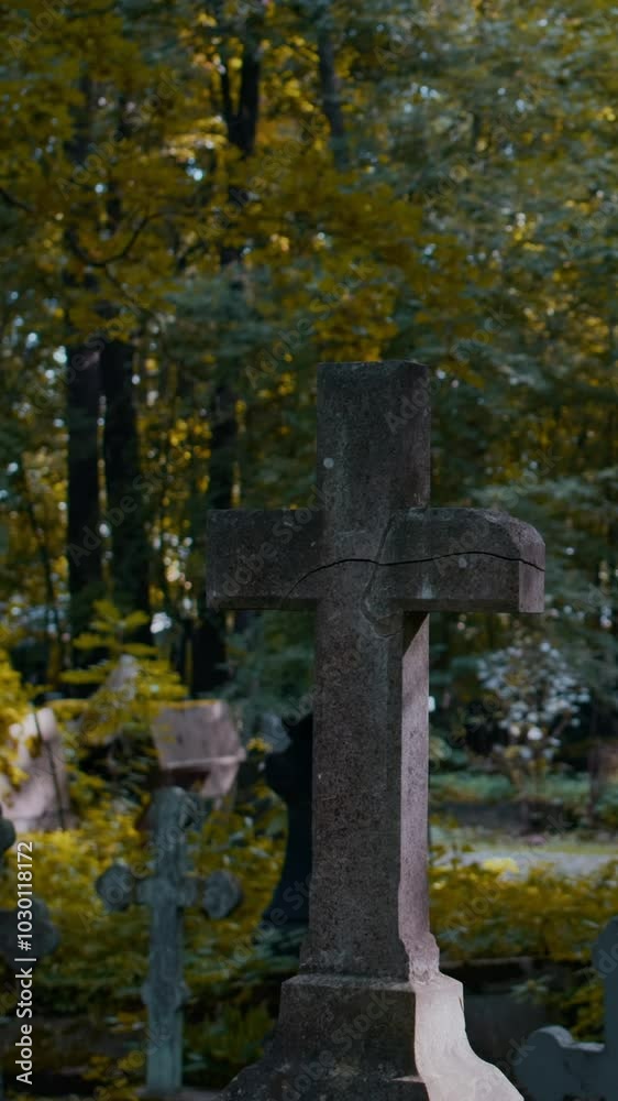 Vertical no people shot of old memorial cross on grave in cemetery with golden-leafed trees in background on autumn day Vertical no people shot of old memorial cross on grave in cemetery with golden-leafed trees in background on autumn day