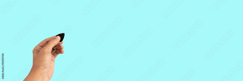 Black male hand holding a guitar pick isolated on ccyan background banner Black male hand holding a guitar pick isolated on ccyan background banner