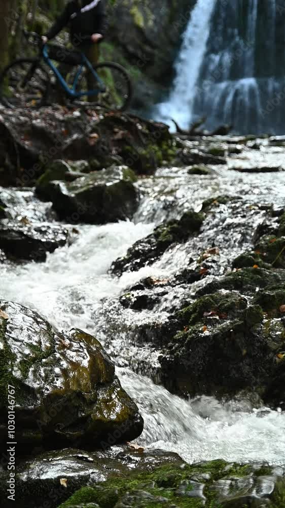 Vertical shot of cascading waterfalls and the lower body of a biker, slow motion Vertical shot of cascading waterfalls and the lower body of a biker, slow motion