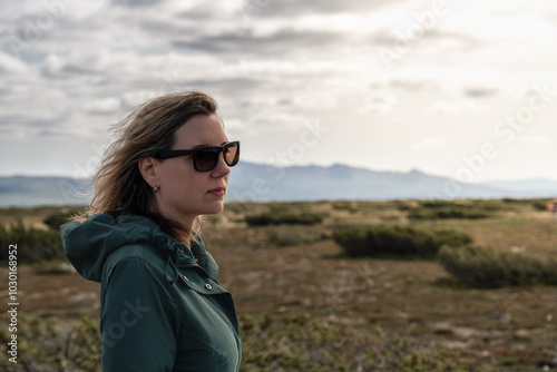 Woman in Sunglasses stands in the expansive Flatruet high fell, facing the majestic mountains, her hair blowing gently in the wind, bright glowing sunlight on her face. Enjoying the beauty of Sweden