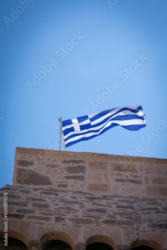 Greek flag waving on a historic stone building against a clear blue sky