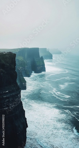 Rugged cliffs meet turbulent waves on a misty day at the shoreline
