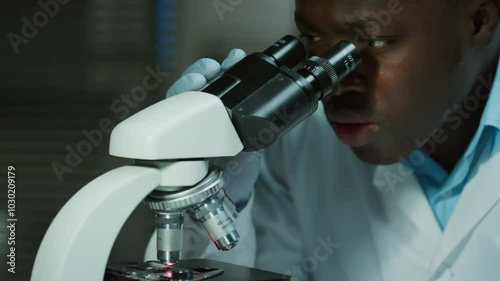 African American male scientist in medical gloves examining specimen under microscope while working in laboratory photo